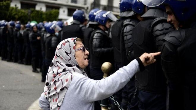 GETTY IMAGES Image caption Пожилая женщина разговаривает с полицейскими алжирских спецподразделений во время недавних протестов