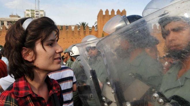 GETTY IMAGES Image caption Мирные протесты с большей долей вероятности привлекают на свою сторону население. На снимке - участница демонстрации в поддержку реформ перед бойцами сил безопасности в Марокко (2011 г.)
