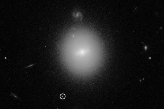 NASA / ESA / D. LIN (UNH) Image caption Обнаруженная черная дыра (обведена кружком) находится на окраине отдаленной галактики
