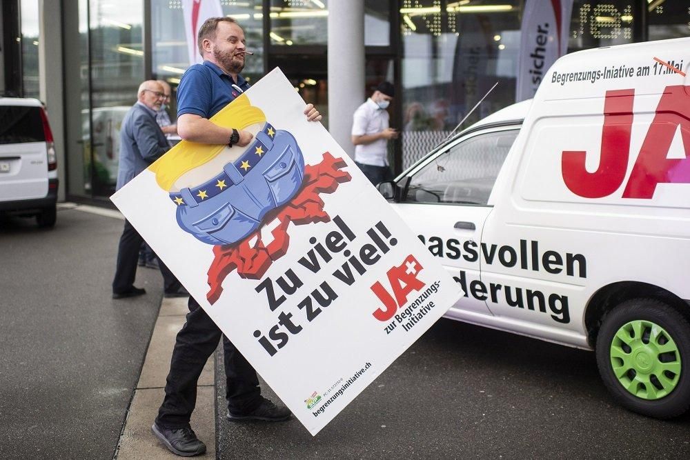 "Это слишком много!" - написано на плакате, который держит сторонник инициативы "За соразмерную миграцию". Фото: EPA