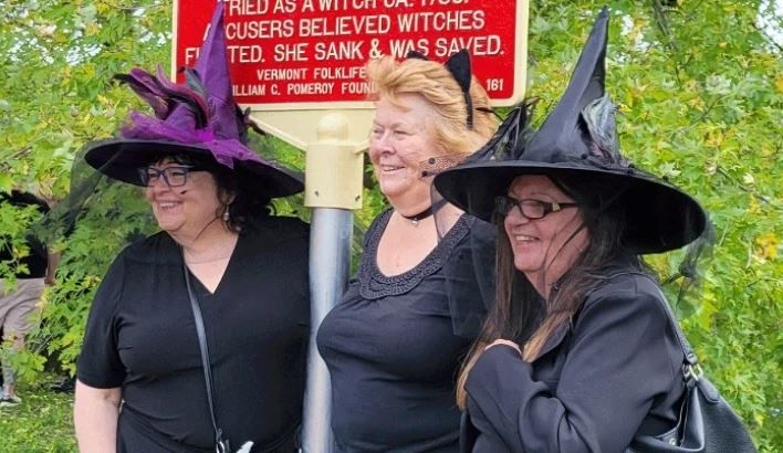 На этой фотографии изображены люди, одетые как ведьмы, собравшиеся возле недавно установленного исторического указателя в Вермонте, посвященного памяти жерт суда пнад ведьмами.